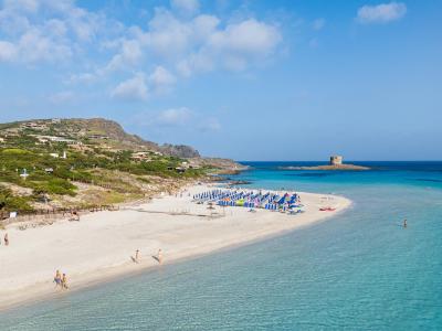 Sandstrand mit türkisfarbenem Meer und entferntem Turm.