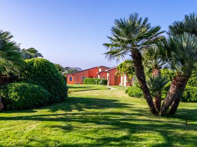 Red house with green garden and palm trees under blue sky.