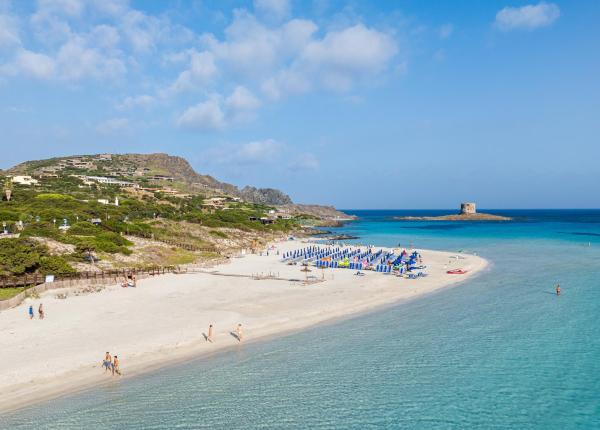 Sandstrand mit türkisfarbenem Meer und entferntem Turm.